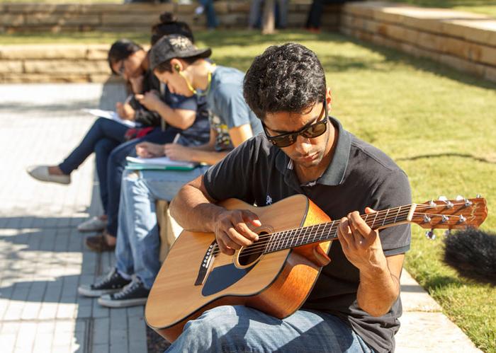 A student playing an acoustic guitar at TI Plaza