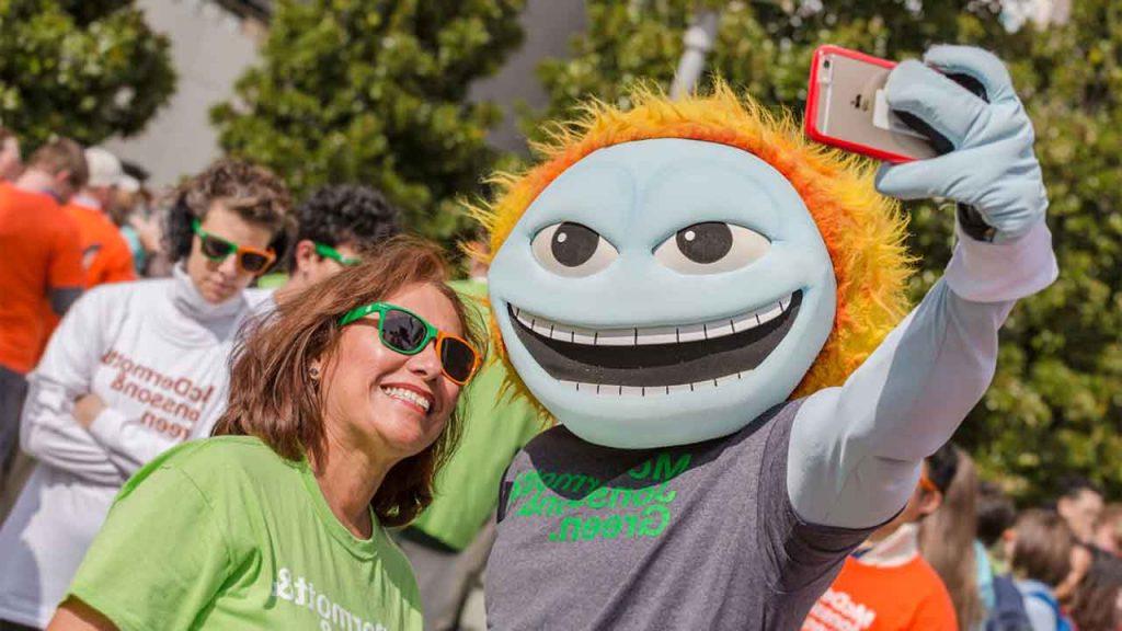一名戴着橙绿墨镜的工作人员与犹他大学吉祥物Temoc自拍.