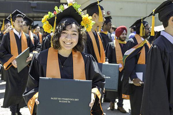 A student in graduation regalia holds a diploma holder outside of the Activity Center.